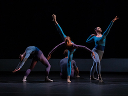 Against a dark background, a group of dancers perform on stage.