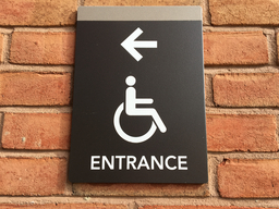 Campus Accessible Entrance Sign with directional arrow on a UMBC brick wall