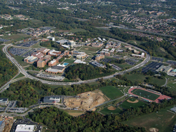 Ariel photo of UMBC's main campus, both academic and residential buildings, within Hilltop Circle. The Research Park and Athletic Fields are in the foreground