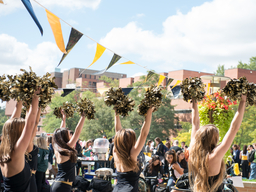 UMBC Dance Team with black and gold pom-poms raise their arms and cheer on UMBC campus.