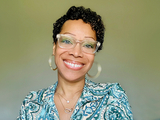 Human wearing glasses, hoop earrings, and a blue patterned shirt.