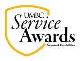 UMBC Service Awards logo with a gold shield outline. The text inside the shield is black and says "UMBC Service Awards" in a mix of serif and script-like fonts. Below "Service Awards" are the words "Purpose & Possibilities.